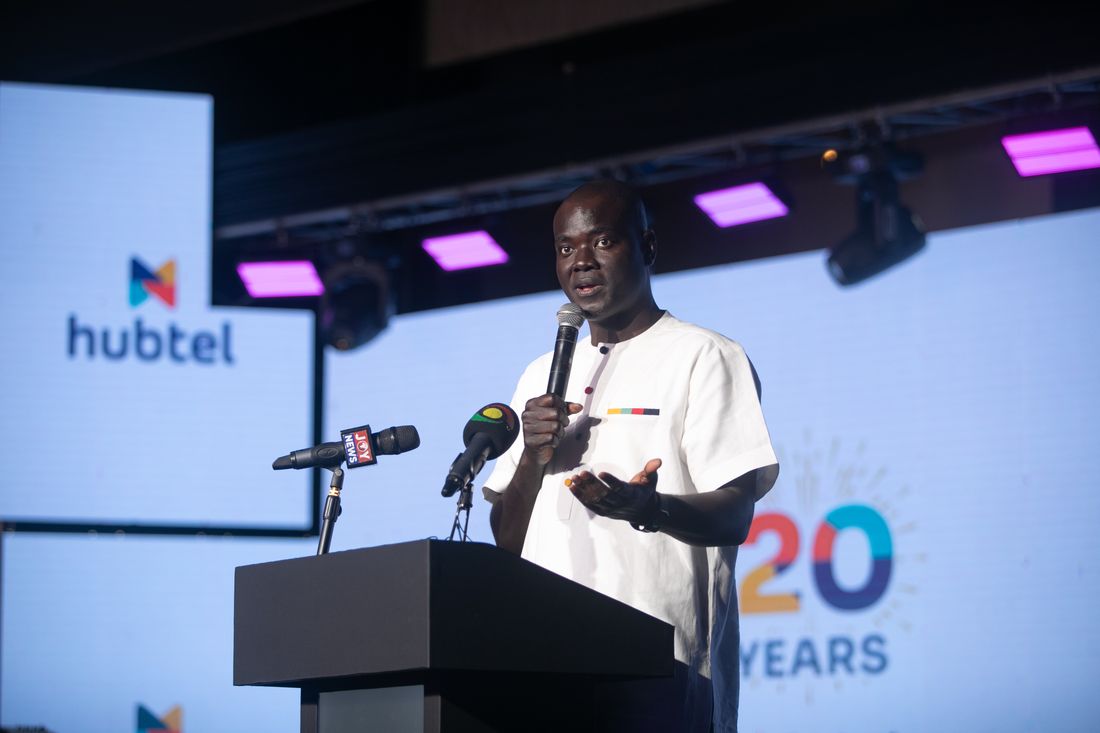 Alex Bram speaking at the podium with the Hubtel logo and 20 Years branding on screen